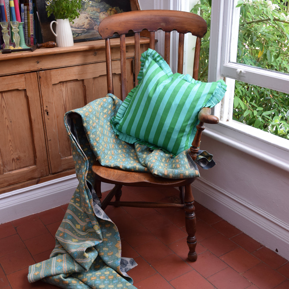 Hand Block Print Striped Frilled Cushion with Feather Insert – Green & Mint lifestyle shot styled on a vintage wooden chair with a draped teal Kantha quilt, showing the bold green and mint stripe cushion with matching green and mint pleated frill