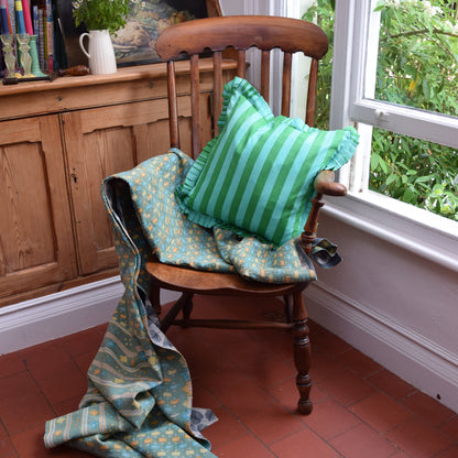 Hand Block Print Striped Frilled Cushion with Feather Insert – Green & Mint lifestyle shot styled on a vintage wooden chair with a draped teal Kantha quilt, showing the bold green and mint stripe cushion with matching green and mint pleated frill