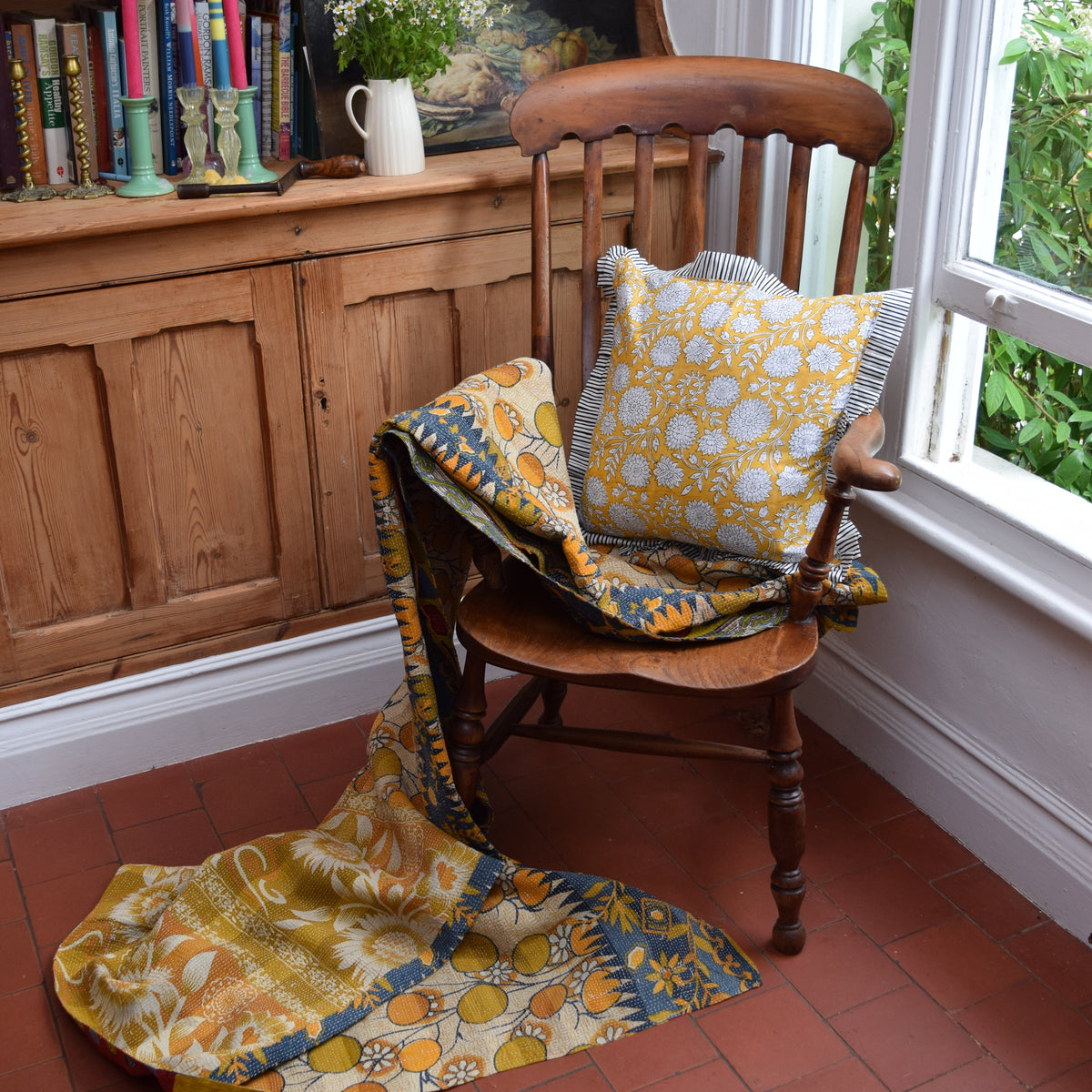 Hand Block Print Dahlia Cushion with Stripe Frill & Feather Insert – Saffron lifestyle shot styled on a vintage wooden chair with a draped floral Kantha quilt, showing the bold saffron yellow dahlia cushion with black and white candy stripe pleated frill