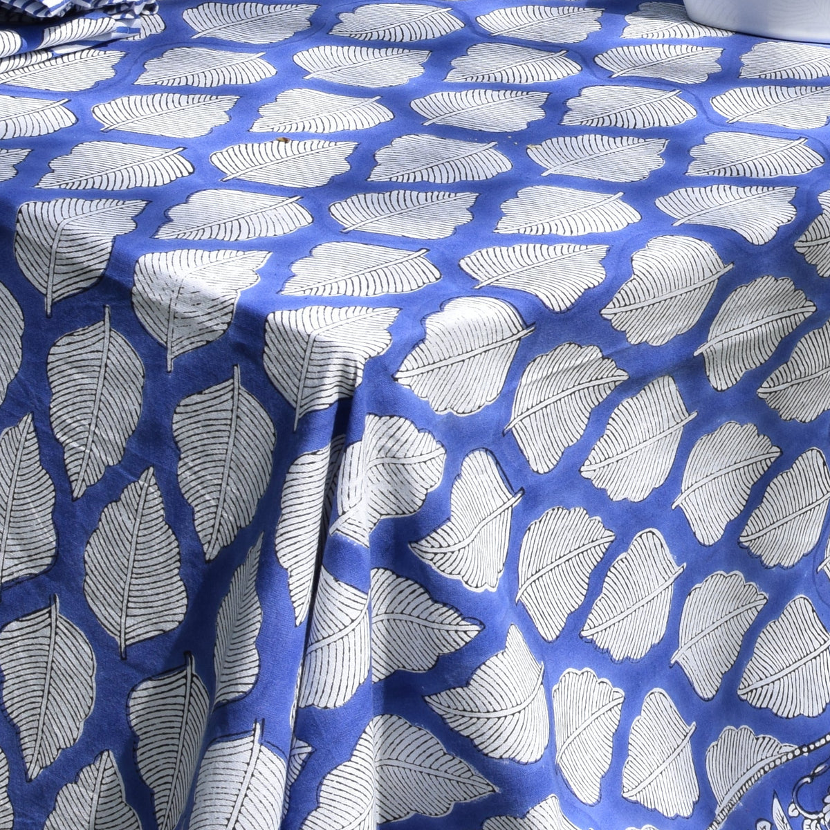 Hand Block Print Cotton Tablecloth – Bold Leaf close detail showing the all-over bold white leaf block print repeat on deep blue cotton, with the corner fall and drape of the tablecloth visible in bright garden sunlight