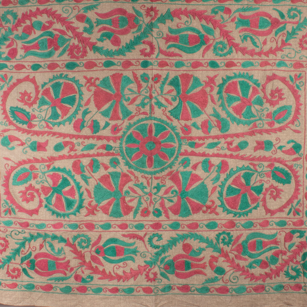 Vintage Hand Embroidered Linen Suzani – Minimalist Elegance & Restraint close-up detail showing the bold two-tone hand embroidery in coral pink and teal green, with a central circular medallion flanked by large wheel rosettes, interlocking geometric petal forms, and scrolling foliate borders, all on a warm vintage linen ground
