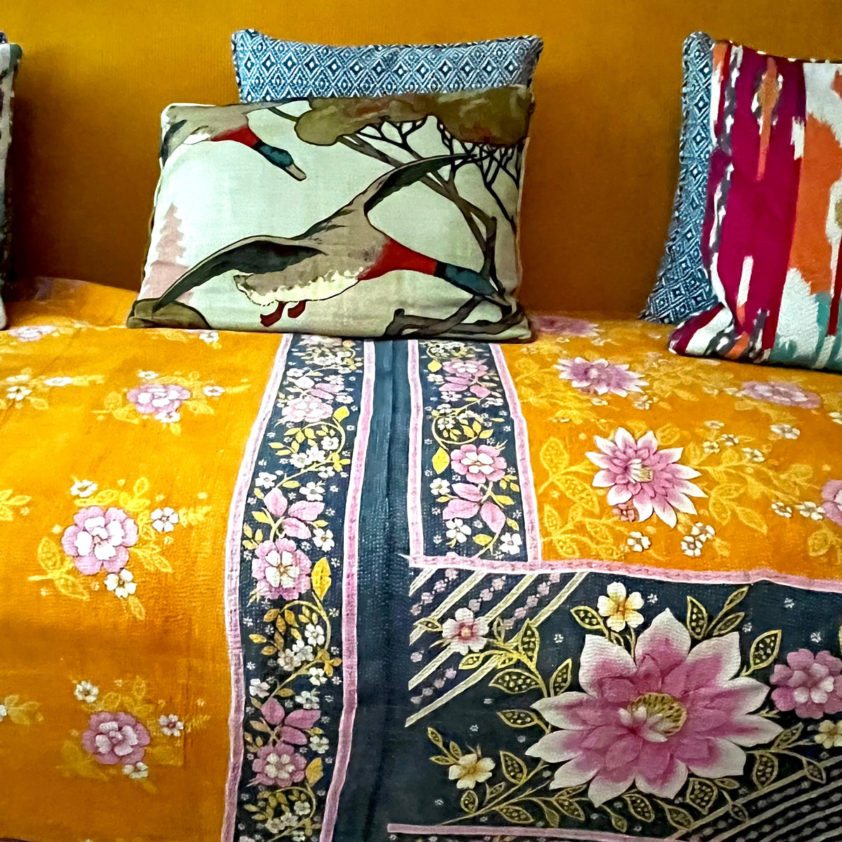Handcrafted Vintage Kantha Quilt – In Full Bloom draped over a sofa, showing vibrant pink and white dahlias on rich sunshine orange with black floral border