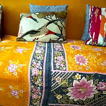 Handcrafted Vintage Kantha Quilt – In Full Bloom draped over a sofa, showing vibrant pink and white dahlias on rich sunshine orange with black floral border