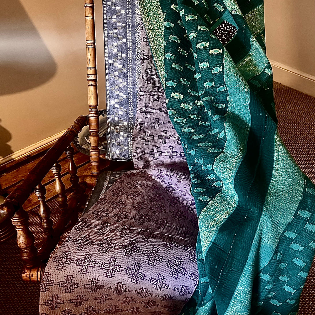 Handcrafted Vintage Kantha Quilt – Purple Aqua Ocean Haze lifestyle scene draped over a vintage wooden rocking chair showing both reversible sides — soft purple cross motif and rich ocean teal with decorative Kantha stitching